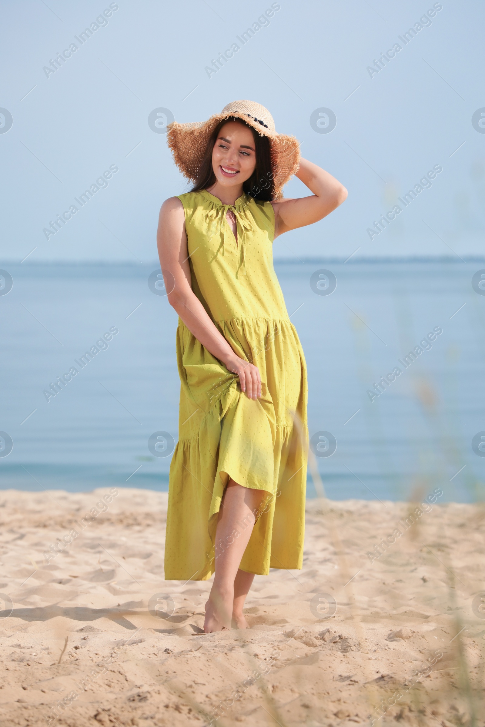 Photo of Beautiful young woman wearing straw hat on beach. Stylish headdress