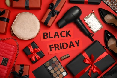 Photo of Gift boxes, cosmetics, hairdryer, shoes, women's accessories and phrase Black Friday on red background, flat lay