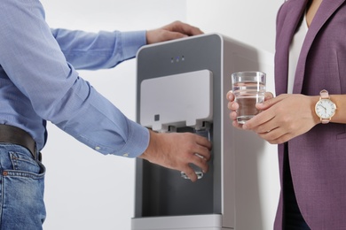 Photo of Employees taking glasses of water from cooler in office, closeup
