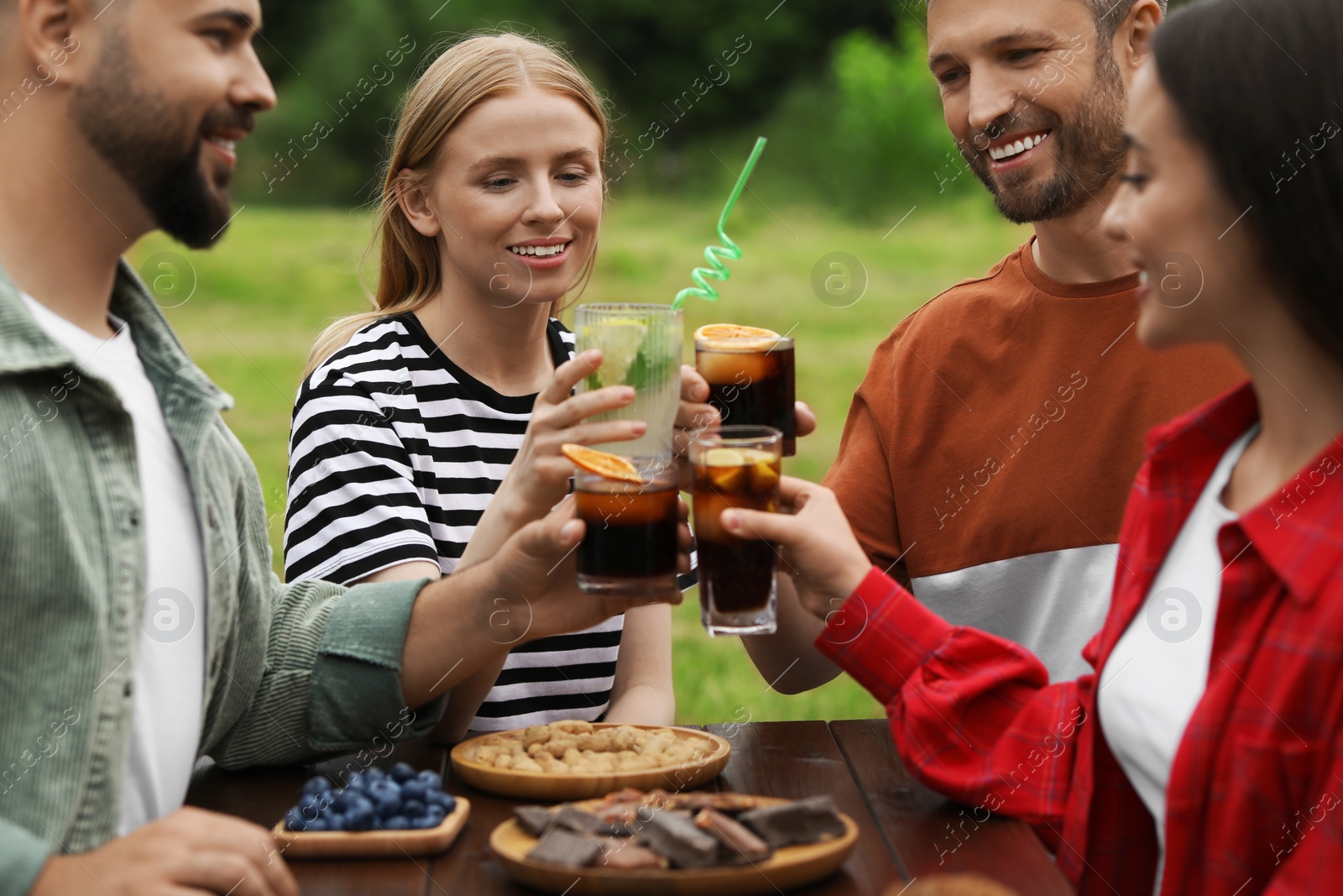 Photo of Happy friends clinking glasses with cocktails at table outdoors