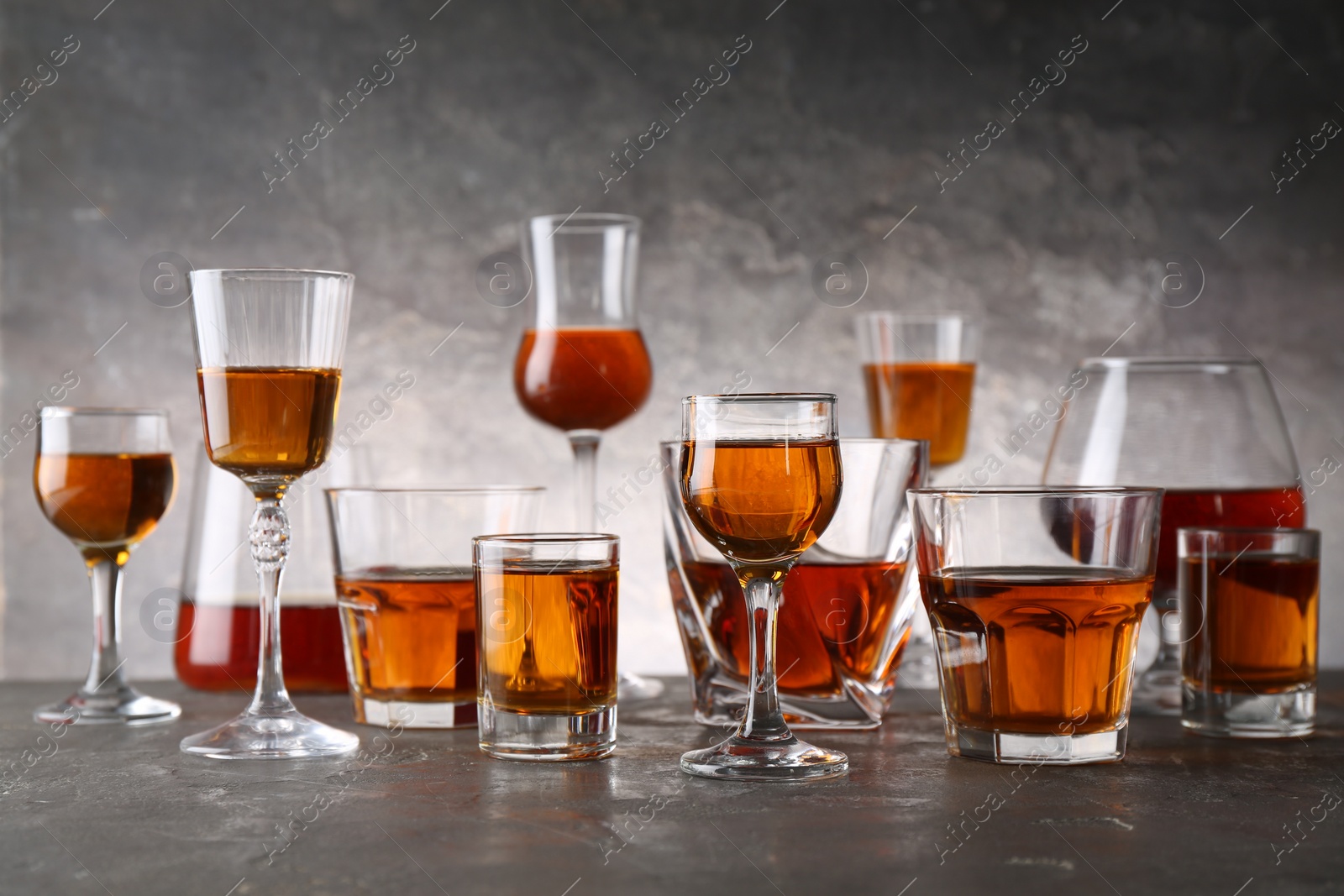 Photo of Different delicious liqueurs in glasses on grey table