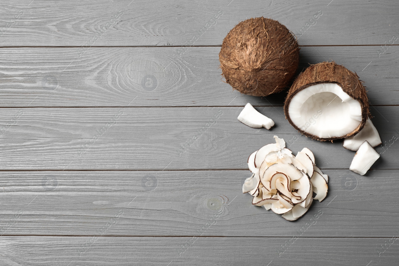 Photo of Flat lay composition with tasty coconut chips on grey wooden table. Space for text