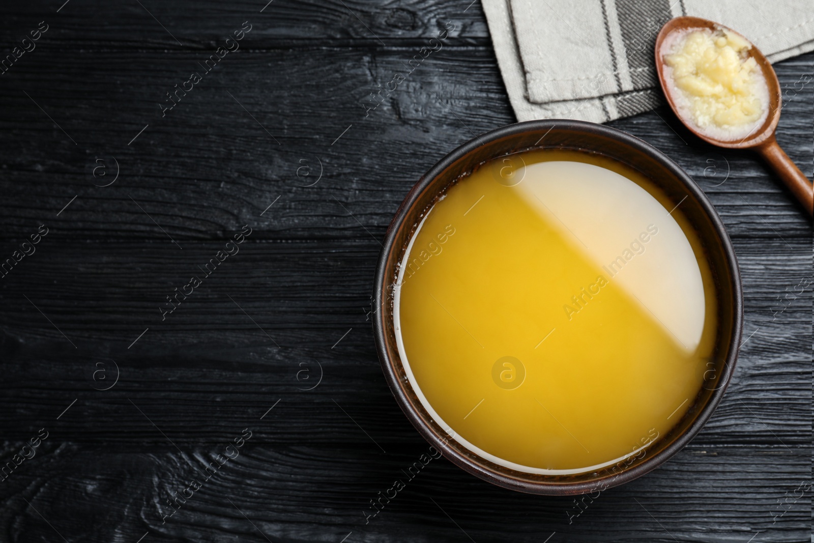 Photo of Bowl and spoon of Ghee butter on dark wooden table, flat lay. Space for text