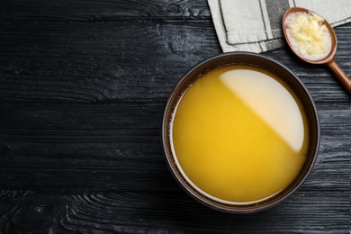 Bowl and spoon of Ghee butter on dark wooden table, flat lay. Space for text