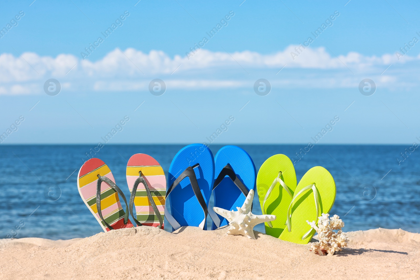 Photo of Composition with bright flip flops on sand near sea in summer. Beach accessories