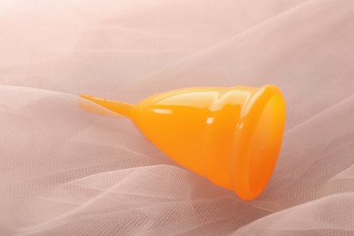 Orange menstrual cup on pink fabric, closeup