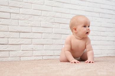 Cute little baby crawling on carpet near brick wall, space for text