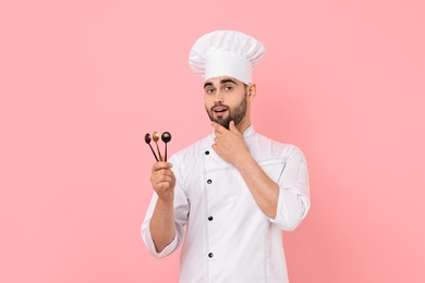 Professional chef holding kitchen utensils on pink background