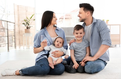 Photo of Happy couple with children sitting on floor at home. Family weekend