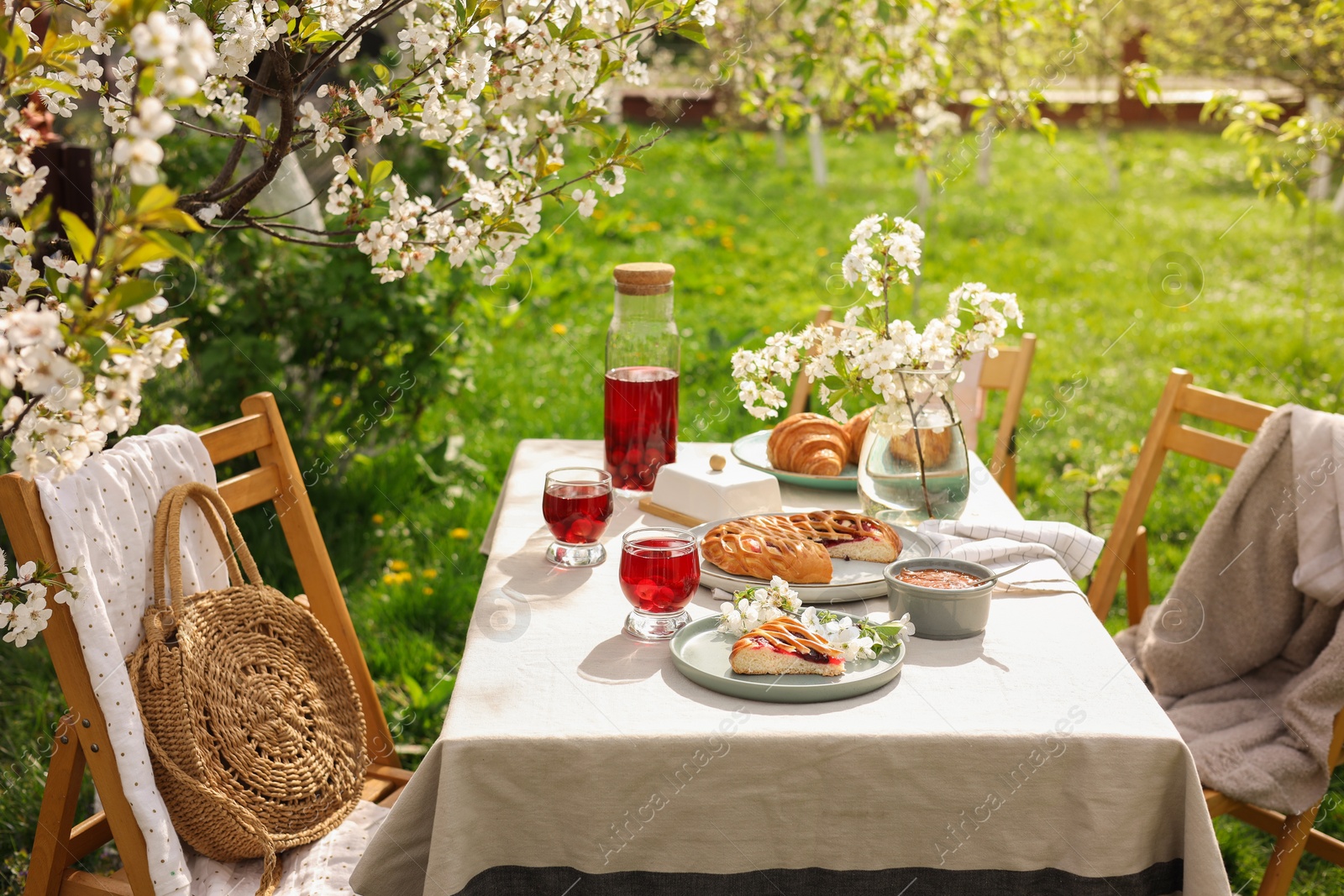 Photo of Stylish table setting with beautiful spring flowers, fruit drink and pie in garden