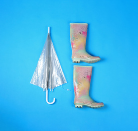 Photo of Beautiful transparent umbrella and rubber boots on blue background, flat lay