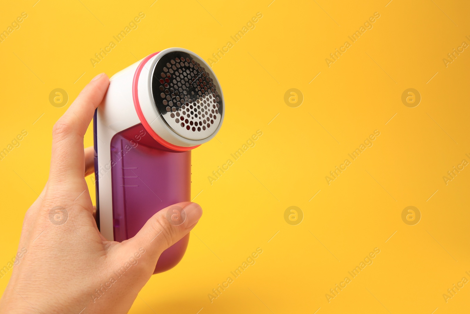 Photo of Woman holding modern fabric shaver on yellow background, closeup. Space for text