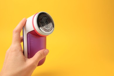 Woman holding modern fabric shaver on yellow background, closeup. Space for text