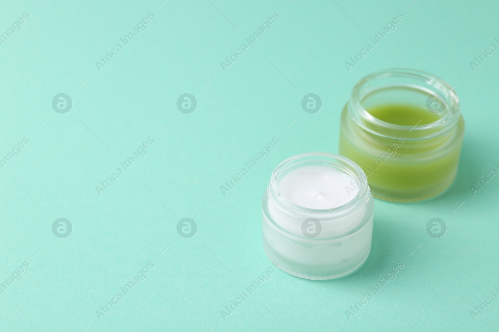 Photo of Moisturizing cream in open jars on turquoise background, space for text. Body care product