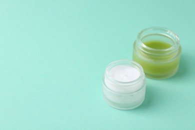 Photo of Moisturizing cream in open jars on turquoise background, space for text. Body care product