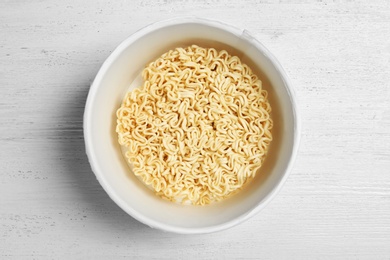 Cup of instant noodles on white wooden background, top view