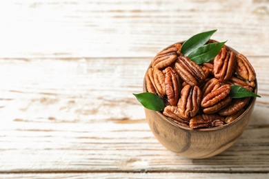Photo of Shelled pecan nuts in bowl on wooden table. Space for text