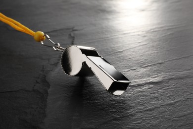 Photo of Referee equipment. Metal whistle on black textured background, closeup and space for text