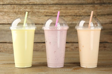 Plastic cups with different tasty smoothies on wooden table