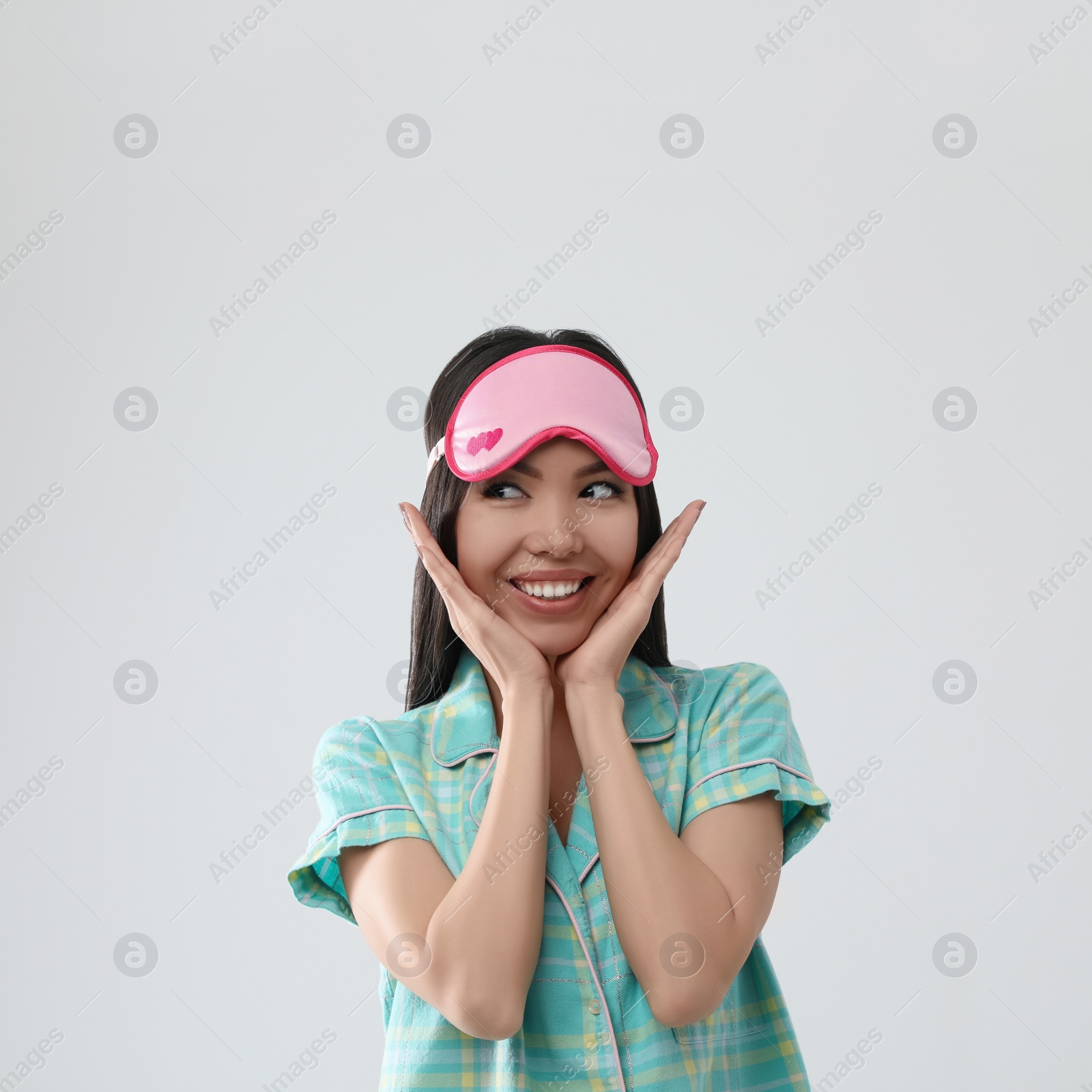 Photo of Beautiful Asian woman wearing pajamas and sleeping mask on light grey background. Bedtime