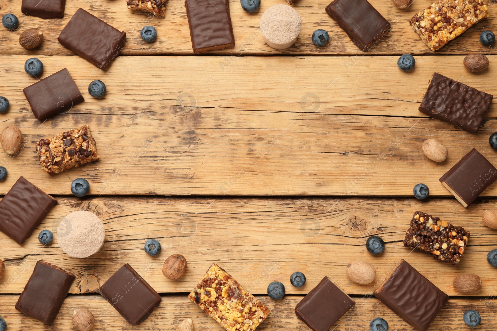 Photo of Frame of different energy bars, nuts, blueberries and protein powder on wooden table, flat lay. Space for text