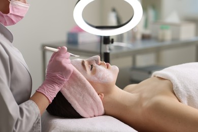 Photo of Cosmetologist applying mask on woman's face in clinic, closeup