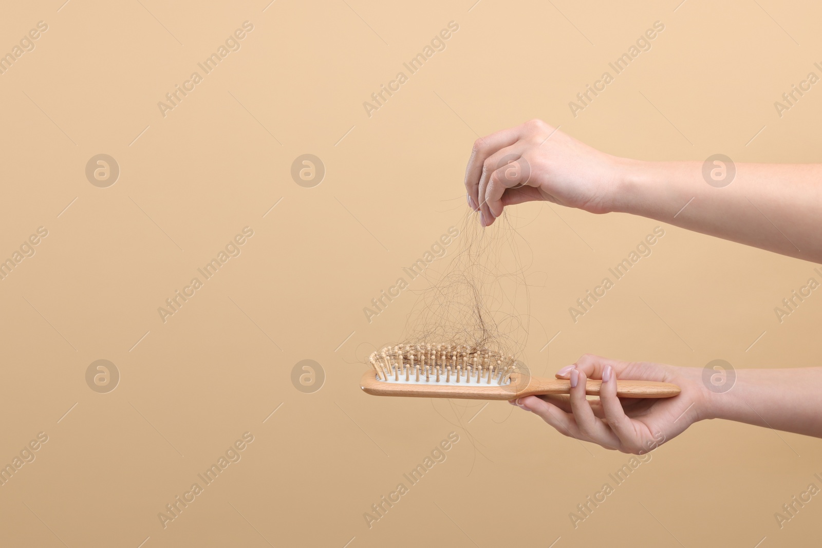 Photo of Woman holding brush with lost hair on beige background, closeup and space for text. Alopecia problem