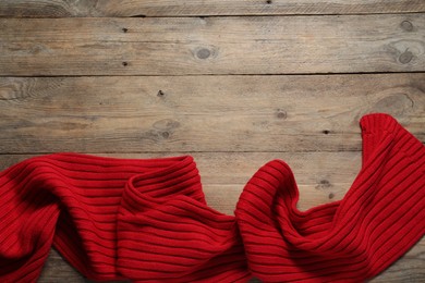 Photo of Red knitted scarf on wooden table, top view. Space for text