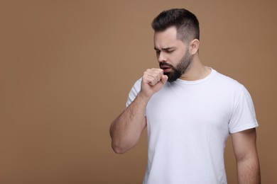 Sick man coughing on brown background, space for text