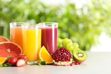 Photo of Three glasses with different juices and fresh fruits on table against blurred background. Space for text