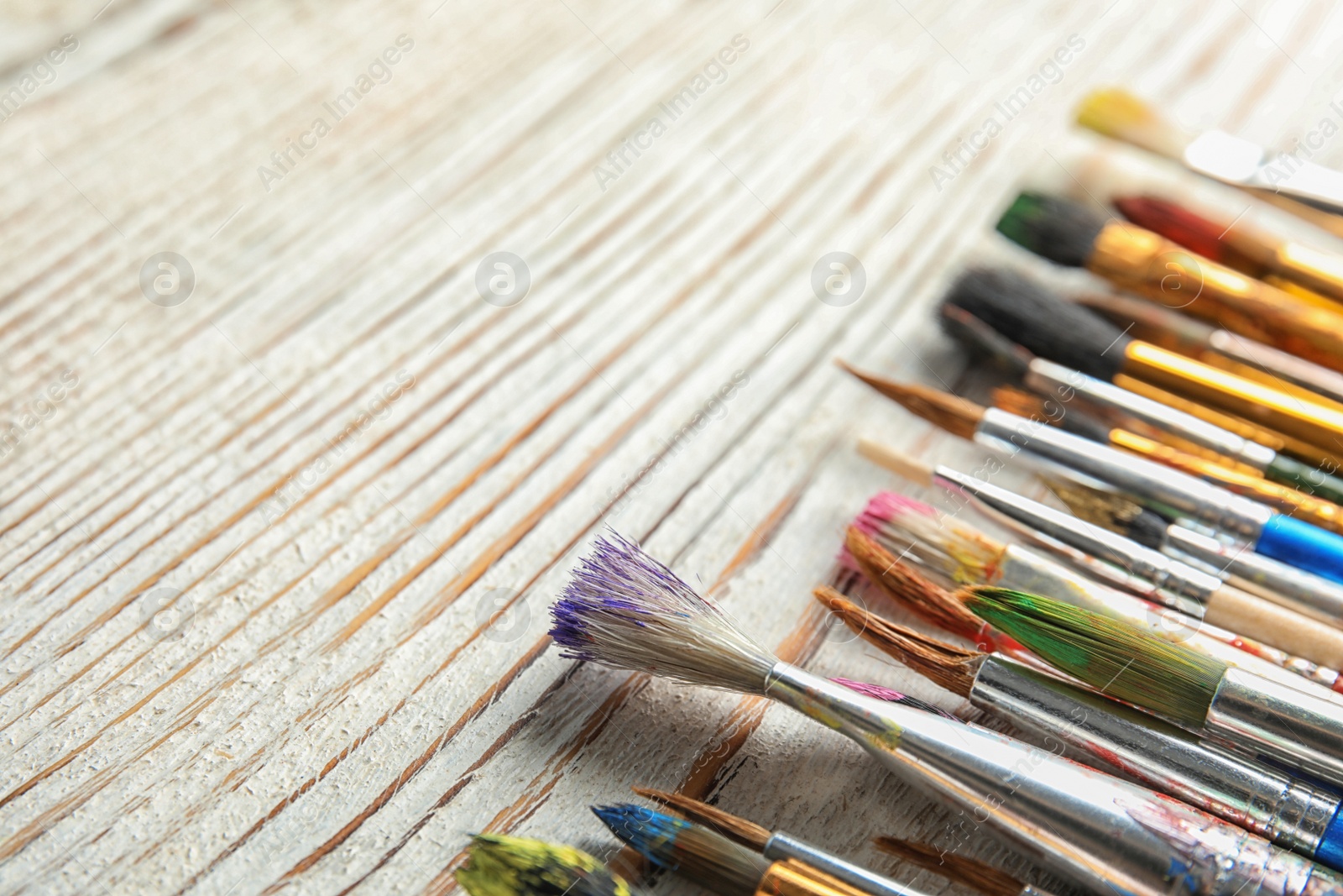 Photo of Different paint brushes on wooden table, closeup. Space for text