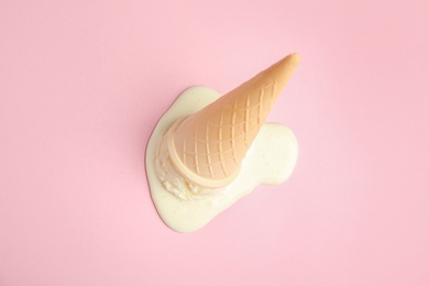 Photo of Melted  vanilla ice cream in wafer cone on pink background, above view