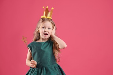 Photo of Cute girl in fairy dress with golden crown and magic wand on pink background, space for text. Little princess