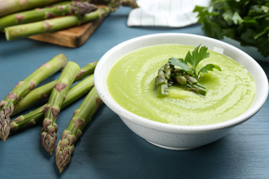 Photo of Delicious asparagus soup served on blue wooden table