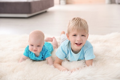 Cute boy with his little sister lying on fur rug at home