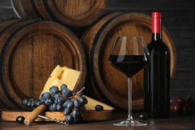 Photo of Delicious wine, wooden barrels, cheese, corkscrew and fresh grapes on table
