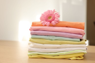 Photo of Stack of clean clothes and pink flower on wooden table