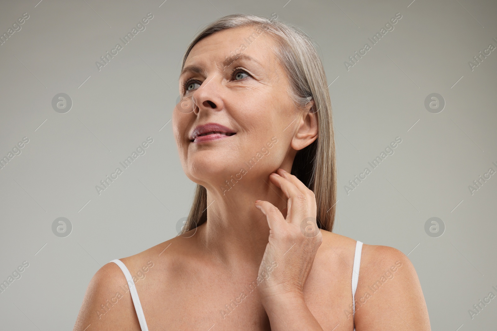 Photo of Beautiful woman touching her neck on grey background, low angle view