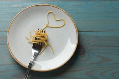 Photo of Heart made of tasty spaghetti and fork on light blue wooden table, top view. Space for text