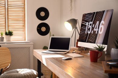 Photo of Modern computer and laptop on wooden desk in room. Interior design