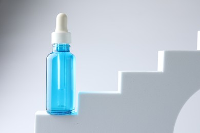 Bottle of luxury serum on stairs against white background