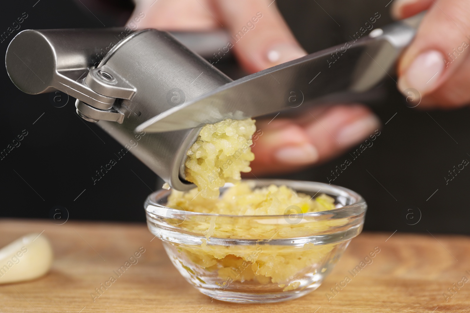 Photo of Woman squeezing garlic with press at wooden table, closeup