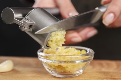 Woman squeezing garlic with press at wooden table, closeup