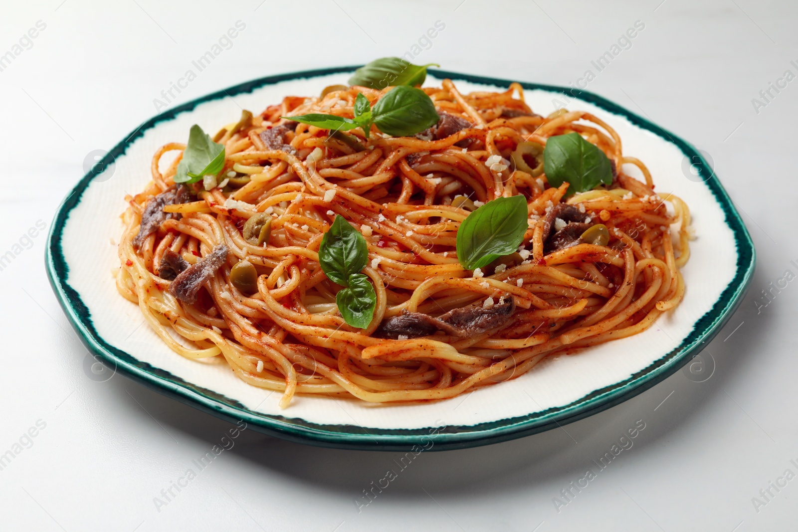 Photo of Delicious pasta with anchovies, tomato sauce and basil on white table