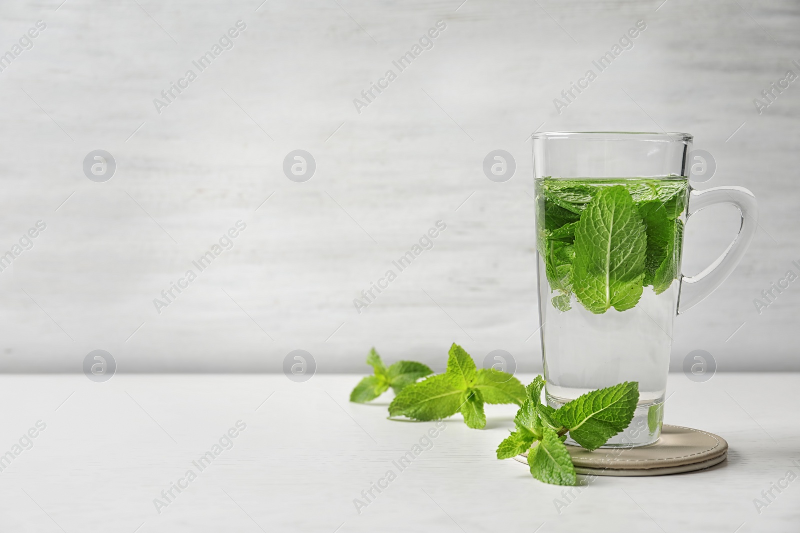 Photo of Cup with hot aromatic mint tea and fresh leaves on table