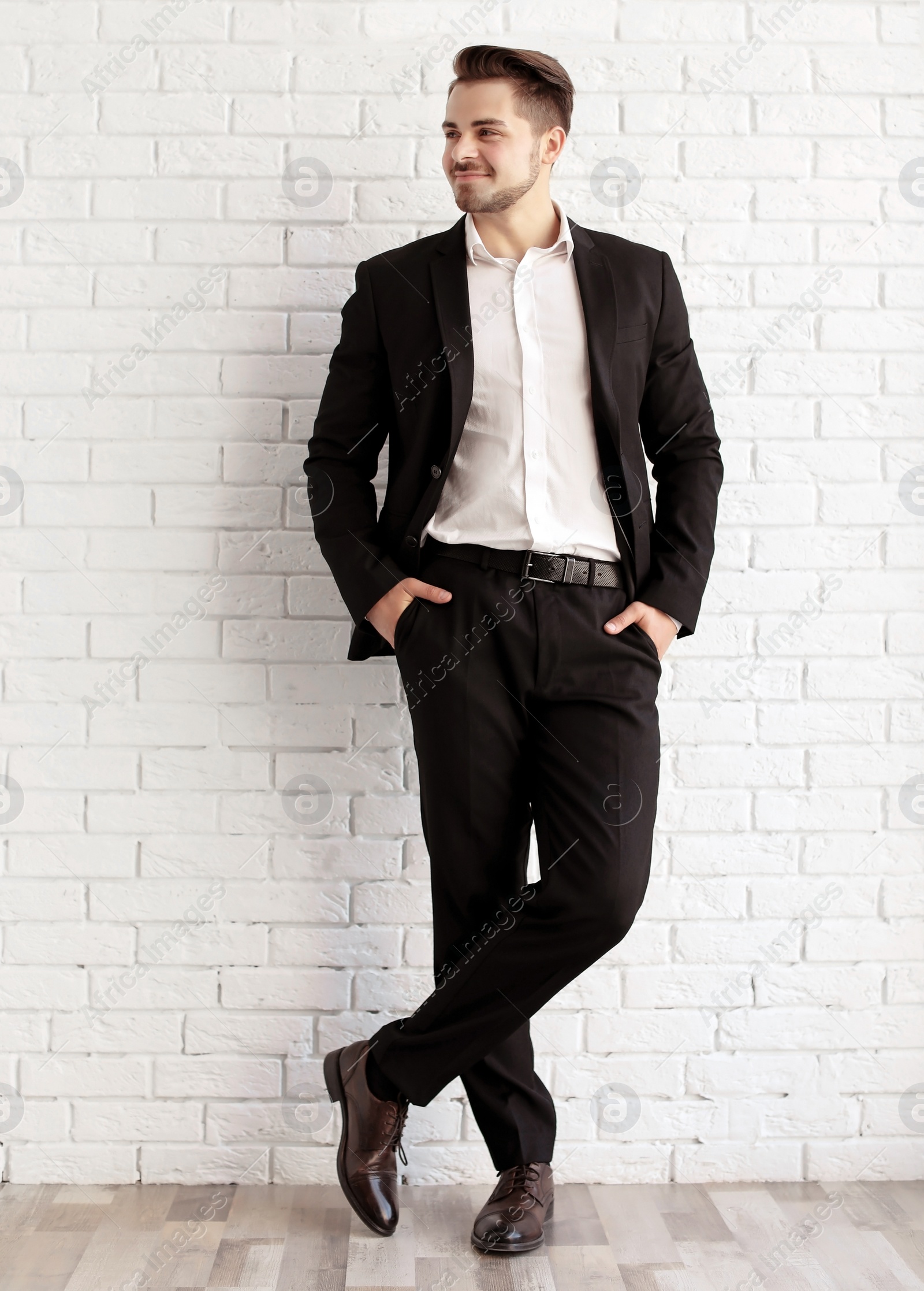 Photo of Handsome young man in elegant suit and leather shoes near brick wall