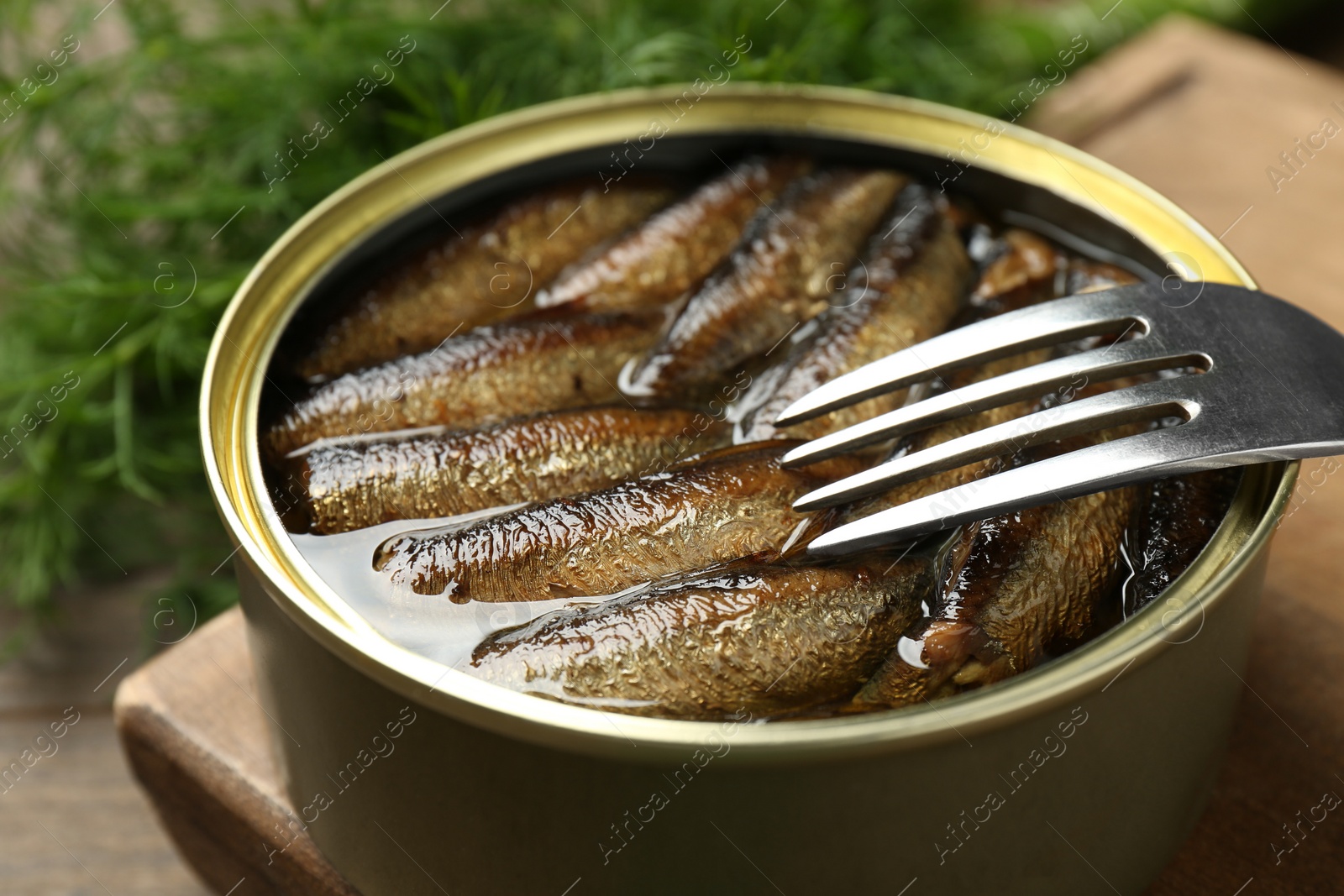 Photo of Tin can with tasty sprats and fork served on wooden table, closeup