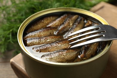 Photo of Tin can with tasty sprats and fork served on wooden table, closeup