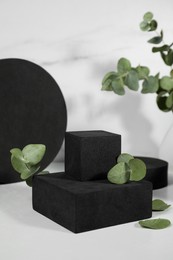 Photo of Black geometric figures and eucalyptus leaves on white marble table. Stylish presentation for product