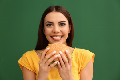 Photo of Young woman eating tasty burger on color background